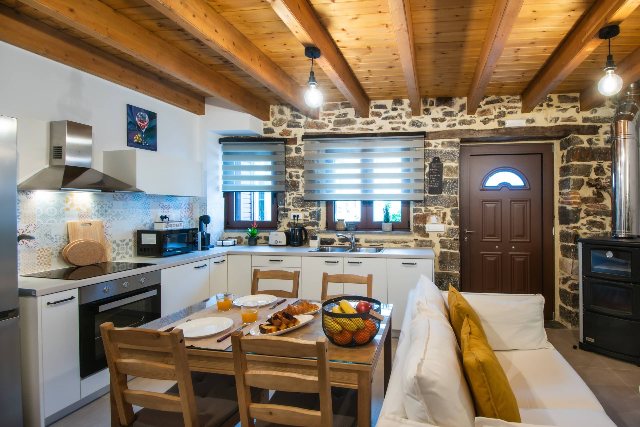 Living space: kitchen, table and sofa under wooden beams, stone wall